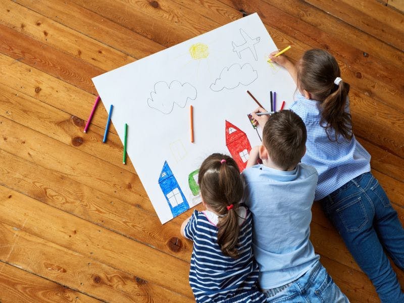 three children colouring houses on paper