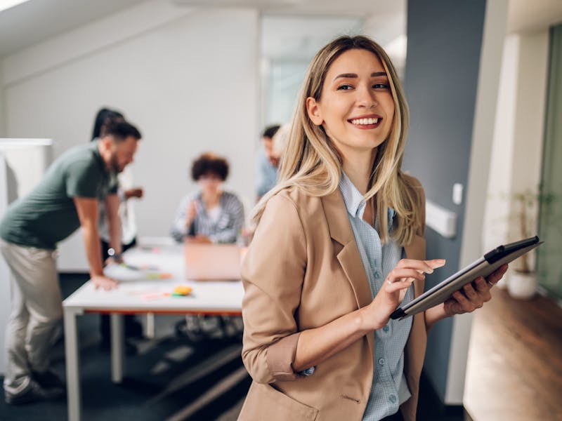 Woman with iPad smiling in tan blazer