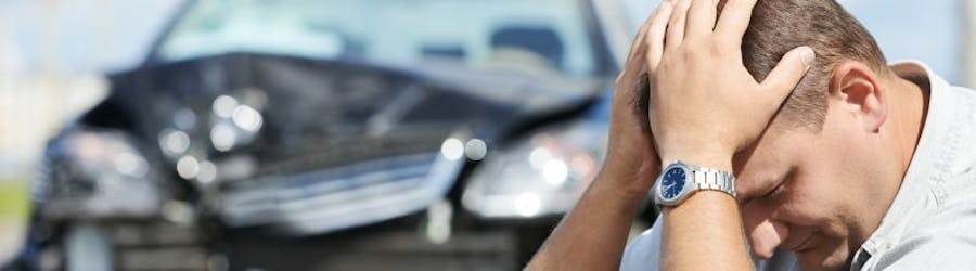 Image of man with head in hands in front of damaged car