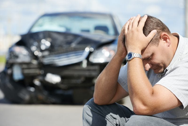 Image of man with head in hands in front of damaged car