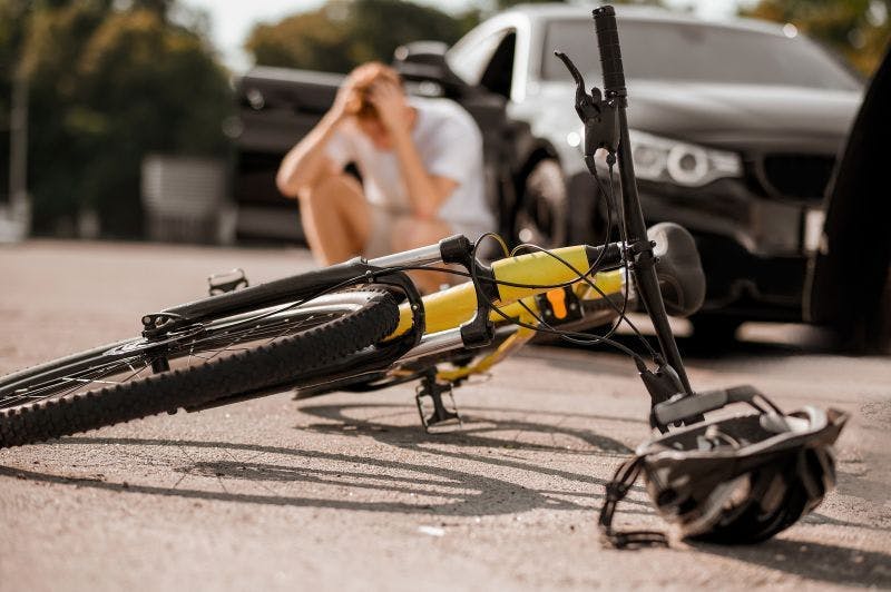 Image of cycle laid on the road in front of a car and driver